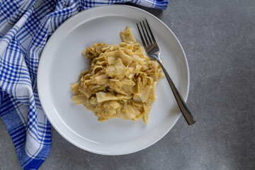 cabbage noodles on a white plate with a fork and blue checkered kitchen towel on grey countertop