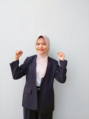 Cheerful Young Asian Professional in Hijab Celebrating Success with Raised Fist in Studio Background
