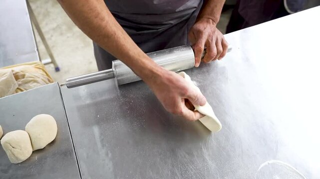 Chef rolls naan dough on metal counter with precision in a traditional Pakistani kitchen. Pakistan