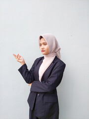 Confident Young Muslim Woman in Hijab and Business Suit Pointing with Hand While Looking Away,...