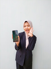 Young Hijabi Entrepreneur Wearing Formal Suit Presenting Mobile Phone Display, Standing Against...