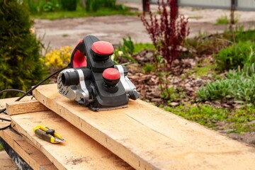 An electric planer is set up on a wooden board outdoors, ready for woodworking and building projects.