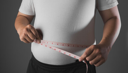 Fototapeta na wymiar Overweight or obese man with abdominal fat using a tape measure to check his waist size, Health and medicine concept He is on a diet and losing weight