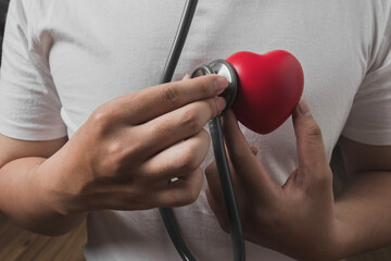 man uses a stethoscope to check the heartbeat. red heart shape exercise ball in hands with doctor...