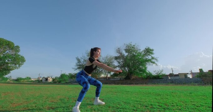 Young woman performing squats in slow motion at park. Outdoor exercises