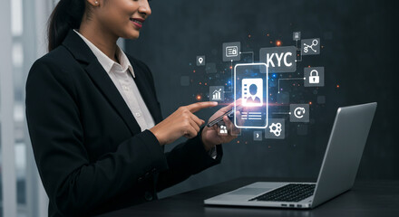 Woman in suit using phone with kyc interface and laptop on desk in front of dark background space 100