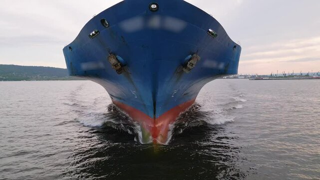 Close-up aerial view of a large cargo ship s bow cutting through the water, creating waves. Maritime transportation and shipping industry scene in motion