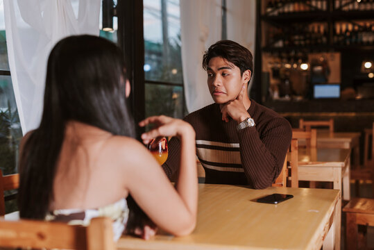 A young Southeast Asian man gives a sarcastic look in response to his date&rsquo;s comment, reflecting tension and passive frustration mid-conversation, or an attitude ego problem.