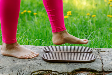 Close-up of a brave unrecognizable woman in pinky leggings who steps barefoot on a Board with nails during a morning practice of siddha yoga.