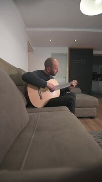Man relaxing at home playing acoustic guitar on sofa