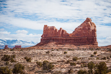 Red rock cliffs and snowy La Sal Mountains beneath a cloudy sky