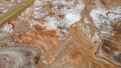 Aerial view of a van driving beside colorful desert cliffs