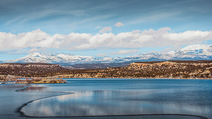 Snow-capped mountains and desert lake with soft cloud reflections