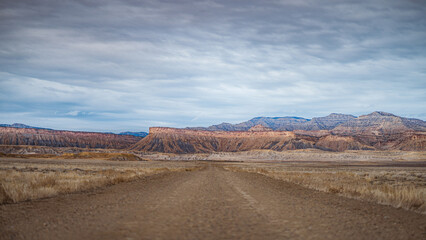 Fototapeta premium Dirt road through dry desert valley with rugged layered cliffs