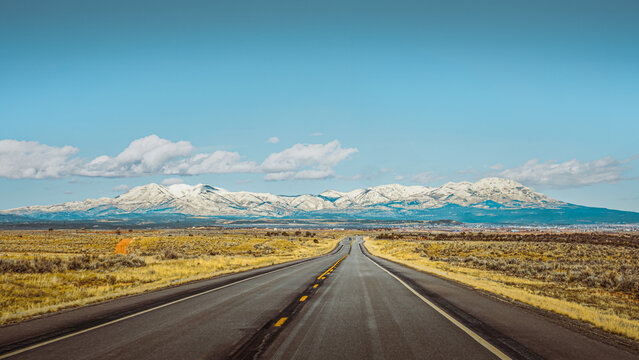 Scenic highway leading toward snow-capped mountains, blue sky