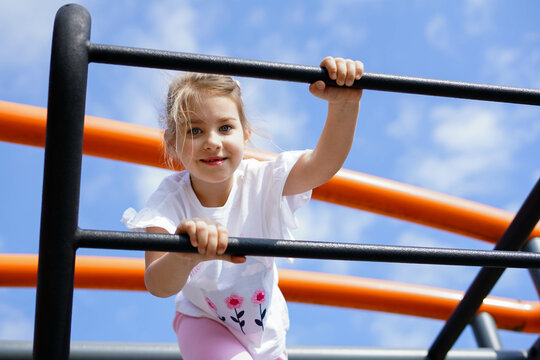 Smiling girl climbing bars at playground under blue sky