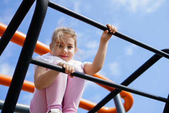 Smiling girl climbing bars at playground under blue sky