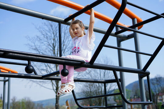 Little girl climbing on jungle gym in playground on a sunny day