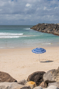 Blue and white beach umbrella on a empty beach with a rock pier