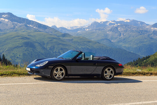 Oberwald, Switzerland - August 11, 2024: Blue Porsche 911 convertible and panorama with mountains at Grimsel Pass road in Swiss Alps.
