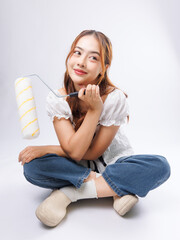 Asian young beautiful woman cheerful confident long curly wavy hair wearing white puff sleeve blouse blue jeans holding paint rollers brush sitting posing on white background renovation room concept.