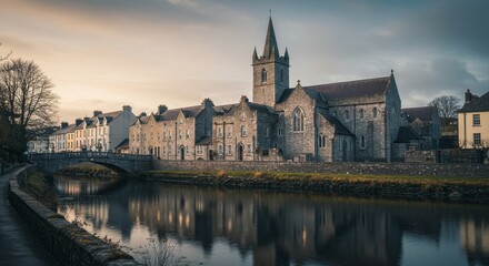 Fototapeta premium Photo of Historic Stone Church Beside River in Town at Sunset
