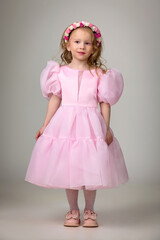 Little cute girl in pink dress, flower wreath and shoes posing in studio on white background