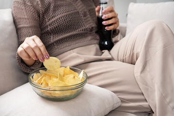 woman eating potato chips and drinking soda, showing emotional eating behavior and unhealthy food choices high in sugar and salt