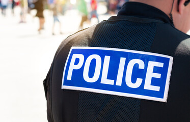 Police officer - close up of policeman on duty from local department near crowd of public in background. Wearing hi-visibility stab proof vest uniform worn by police officers. Officers enforce the law