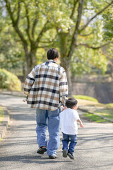 In March, at a sunny forested park in Japan, a 3-year-old Japanese boy walks hand in hand with his father. Captured from behind, this photo shows a quiet and heartwarming moment during a spring walk.