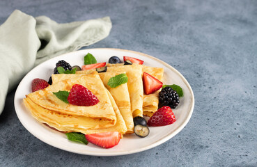 Golden crepes with fresh berries on a blue background. Breakfast. Dessert.