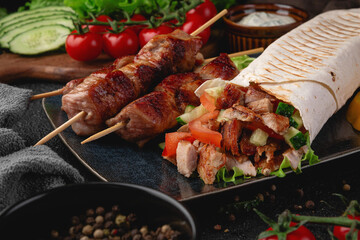 Close-up of grilled pork skewers served with a stuffed shawarma wrap, fresh vegetables like cucumber and tomato, and yellow bell pepper slices. Perfect for restaurant menus and ads