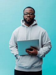 A determined individual, exuding confidence, cradles a laptop, standing against a modern, light-blue backdrop, and capturing an atmosphere of focused work.