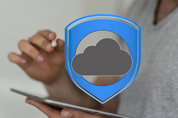 Image of person using tablet with a graphic of a cloud protected by a shield.  Illustrates secure...