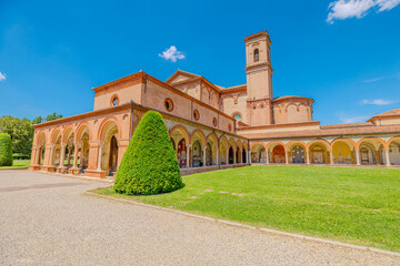 Saint Christopher Church and the large cloister of the Charterhouse of Ferrara, surrounded by cypress trees and a well-kept lawn, stand out against a clear blue sky on a sunny day