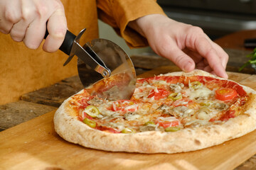 Pizza cutter cuts homemade baked dough. Making pizza with mushrooms and olives