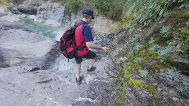 Man crossing mountain river next to crystal clear waterfall at Fuente de Fornos, Badain, Ainsa, Huesca, Aragonese Pyrenees, 4K video with trekking action, wet rock and wild landscape.