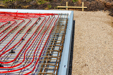 Underfloor heating system with red pipes on construction site, Close-up of underfloor heating installation using red pipes laid on a foundation grid at a building