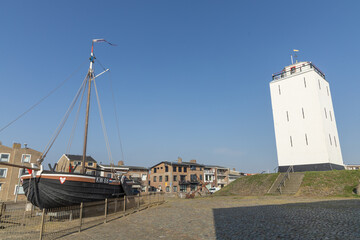 Traditional Dutch fishing boat KW88 on display near the old white lighthouse in Katwijk aan Zee, Netherlands, under a clear blue sky on a sunny day.