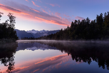 Fototapeta premium Mt Tasman and Mt Cook reflected in the clear waters of Lake Matheson at Sunrise. West Coast. South Island. New Zealand.