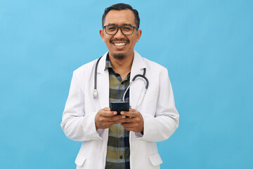 Asian adult male doctor standing while using mobile phone, wearing doctor's coat, hanging...