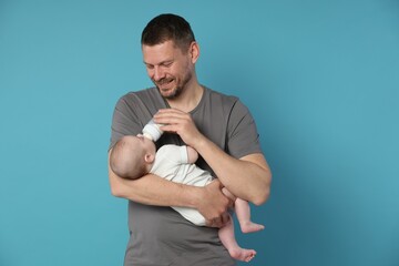 Fototapeta premium Father feeding his little baby with bottle on light blue background