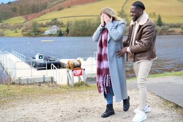 Smiling man with woman covering eyes on riverbank