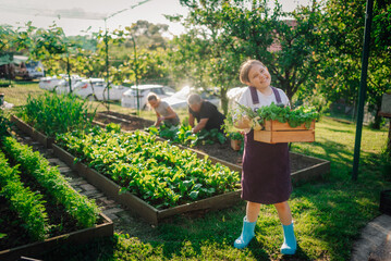 Smiling girl carrying harvested vegetables in family garden