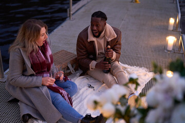 Fototapeta premium Smiling couple in warm clothing enjoying champagne on decorated pier