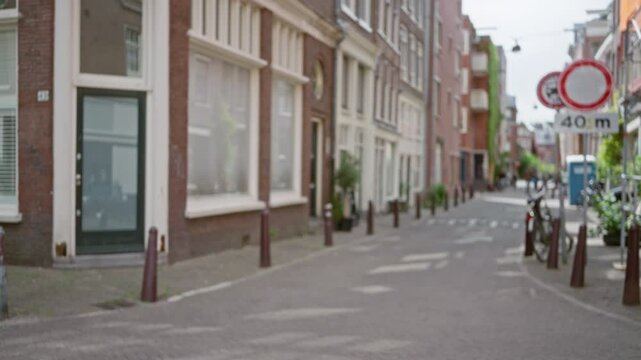 Defocused urban street in amsterdam featuring blurred bicycles and brick buildings under daylight, capturing the quaint charm of a dutch city with a peaceful atmosphere.