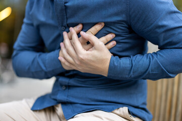 A man clutching his chest, a gesture of pain. Possibly experiencing a heart issue or discomfort,...