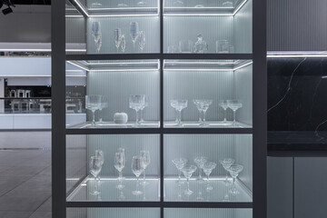 large glass kitchen cabinet with glass doors and shelves, inside cabinet with light. beautiful wine and champagne glasses on shelves. Modern luxury kitchen design. built-in kitchen in minimalist style