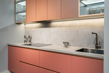 built-in peach-colored kitchen with beautiful facades. Kitchen with upper and lower cabinets, countertop, sink and faucet. Upper cabinets with glass doors. beautiful glasses in cupboards. kitchen unit