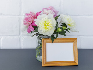 Bouquet of peony flowers in the vase with a photo frame.